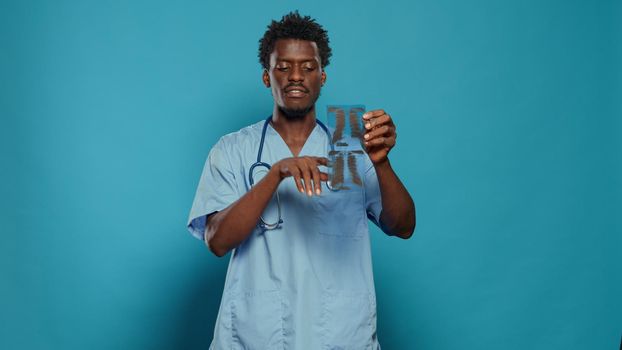 Medical assistant holding x ray scan and explaining disease in studio. Man nurse presenting radiography for diagnosis while wearing uniform and stethoscope for healthcare over background