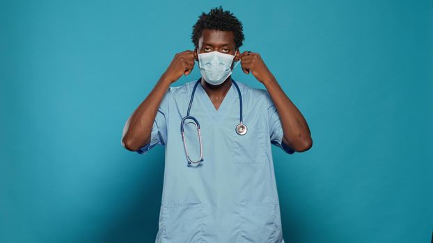 Man nurse wearing face mask for protection against coronavirus pandemic. Medical assistant with protective mask and uniform explaining covid 19 virus prevention, looking at camera.