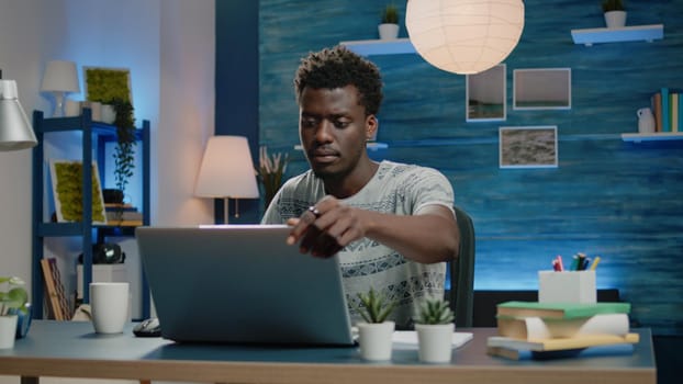 Black adult working from home with laptop and coffee at desk. Businessman of african ethnicity doing remote networking work online. Corporate employee browsing internet for project