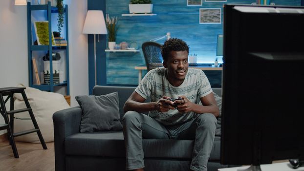 Person smiling after winning video games on television. Adult with controller playing virtual game online on console for entertainment. Gaming man enjoying win on electronic device