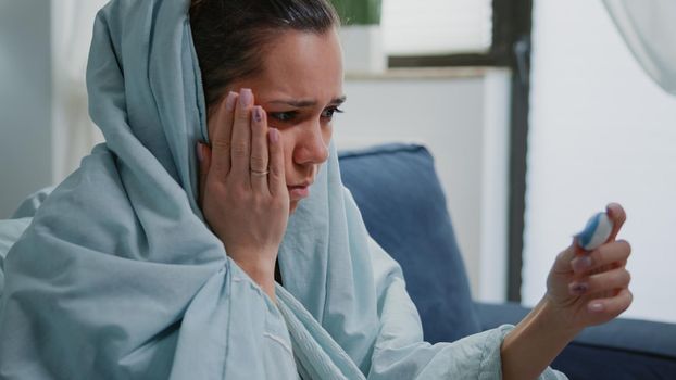 Close up of person with flu looking at thermometer, checking temperature and feeling cold. Woman with coronavirus symptoms holding device for fever measurement and medical diagnosis