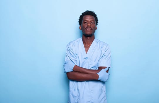 Person working as nurse standing in studio with isolated background. Healthcare specialist wearing uniform and looking at camera with arms crossed. Confident medical assistant