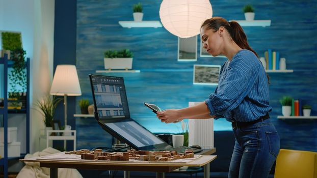 Woman architect analyzing building model on tablet and computer for construction development. Engineer using technology to design blueprint plan for architectural project. Modern architecture