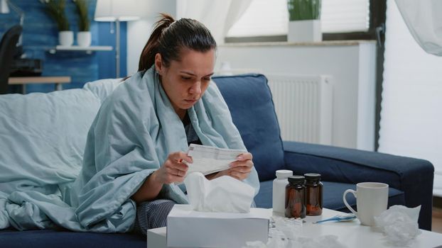 Person with disease infection analyzing package leaflet of pill bottles to cure illness. Woman feeling cold reading medical paper with medication instructions, having medicaments on table