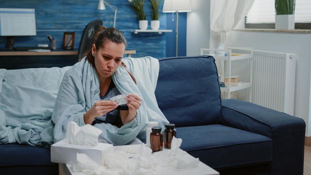 Person reading labels of capsule tablets and bottle with pills for disease treatment at home. Sick adult looking for medicaments and drugs against headache and coronavirus symptoms.