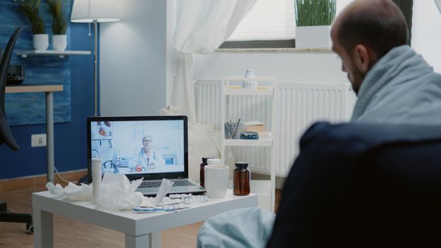 Man with disease using video call for telemedicine, talking to doctor about virus symptoms and treatment against illness. Sick adult with online remote conference asking for medical advice