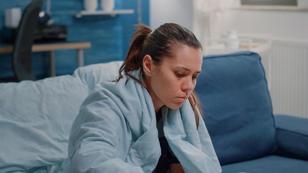 Close up of ill adult looking for medical treatment on table. Sick woman with tablets of medicaments, bottles of pills, box of tissues and thermometer to cure seasonal cold and flu