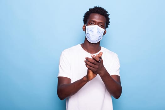 Portrait of african american man clapping and wearing face mask against coronavirus epidemic. Black man applauding while looking at camera. african american adult using hands to applaud in studio