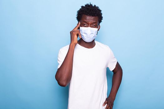 Man with face mask doing thinking gesture in studio. Adult with protective mask against pandemic feeling thoughtful and pensive, standing over isolated background. Concentrated person