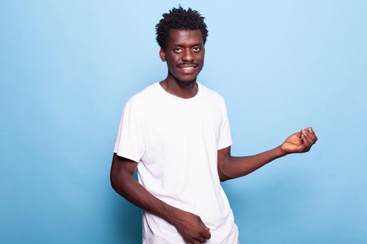 Cheerful person dancing and posing while looking at camera. Portrait of man smiling and having dance party while taking pictures over blue background. Positive adult having fun