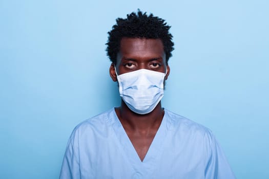Portrait of nurse wearing face mask and uniform standing in studio, working on healthcare. Medical assistant looking at camera, having protection against coronavirus. Man in covid 19 pandemic