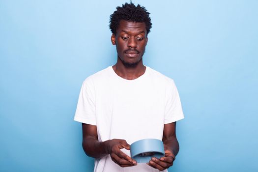 Young adult holding watch in hand and looking at time. Punctual person with worried expression having wall clock and running late. Man in delay watching object with hours and minutes