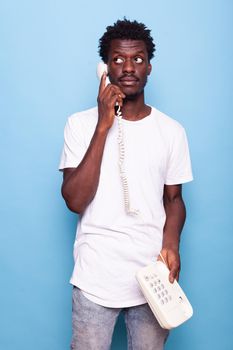 Young adult answering vintage telephone with wire. Man holding retro landline phone and having conversation on phone call. Expressive person with old technology for communication