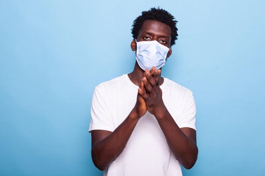 Portrait of adult using hands to applaud and having face mask, standing over isolated background. Casual person with mask for coronavirus protection clapping while looking at camera