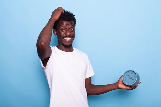 Portrait of man with wall clock holding hand on head, running late to work. Person checking time on watch, feeling alert because of deadline schedule, looking at camera and smiling.