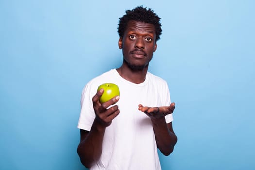 Young adult showing green apple to camera in studio. Portrait of person holding raw fruit with natural vitamins for organic lifestyle. Cheerful man with healthy nutrition and fresh diet