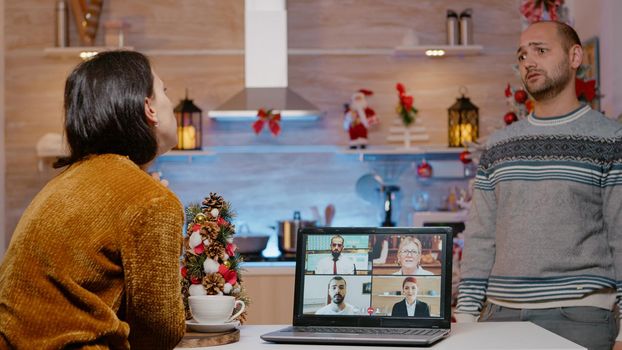 Woman using video call for work meeting on christmas eve while man waiting for holiday celebration at home. Businesswoman working on christmas, couple delaying winter festivity.