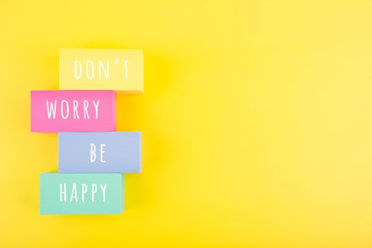 Positive affirmation, mental health or inspiration quote concept. Don't worry be happy hand written on ladder made of multicolored rectangles on yellow background with copy space. Motivational text for inner piece