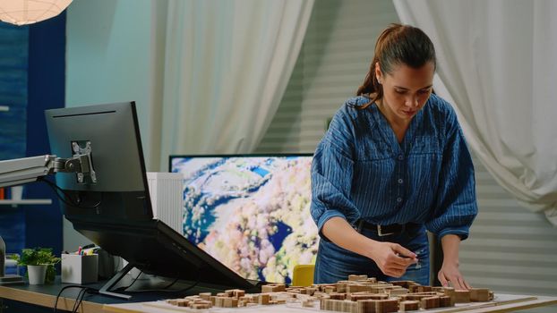 Architect holding maquette in hand using touch screen computer for construction development. Woman engineer analyzing building model and print for architectural layout. Digital architecture