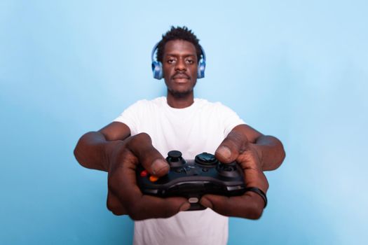 Person holding controller for video games while wearing headphones. Young adult playing game with joystick and listening to music on headset. Modern man having fun with technology.
