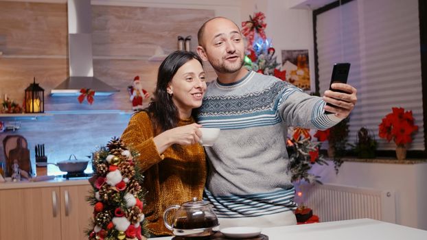 Festive couple talking to relatives on video call conference using smartphone. People holding device while chatting on christmas eve, celebrating holiday with family on remote communication