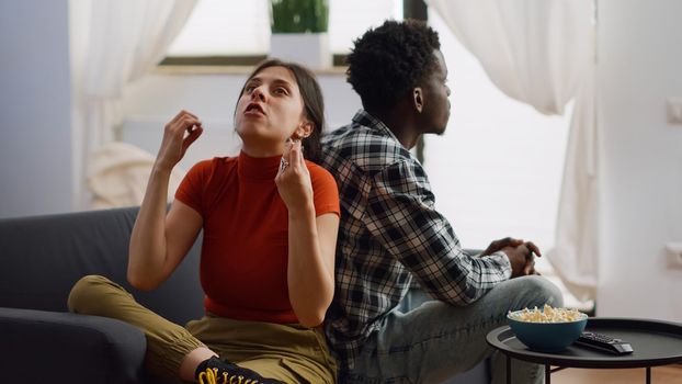Interracial couple shouting at each other having argument in living room. Angry multi ethnic people fighting about marriage issues while sitting together on couch at home. Irritated lovers