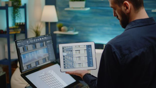 Architect holding digital tablet with building model for construction layout in office. Man engineer working on blueprint plan with touch screen monitor and device for architectural project