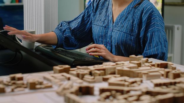 Close up of architectural desk with building model and computer with touch screen. Architect using technology to design maquette for construction development project. Architecture planning