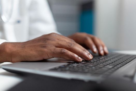 Closeup of african american doctor hand typing healthcare treatment on laptop computer keyboard after analyzing sickness expertise. Practitioner working in hospital office. Health care service