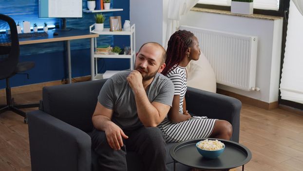 Interracial couple with dispute and marriage problems yelling on couch in living room. Multi ethnic husband and wife having argument fighting at home. Angry partners in fight