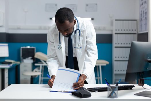 African american therapist doctor analyzing medical documents checking medicine prescription during clinical appointment. Practitioner working at sickness expertise in hospital office