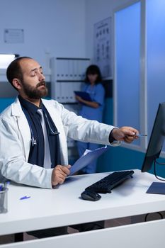 Focused doctor pointing at computer for analysis work at night. Medical specialist analyzing at monitor for healthcare information and practice. Man working as physician at office