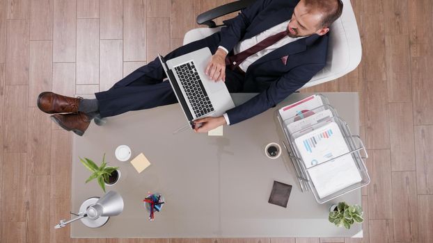 Top view of businessman keeping his feet on desk while typing management statistics planning company investments. Executive manager working at business strategy analyzing online profit in office