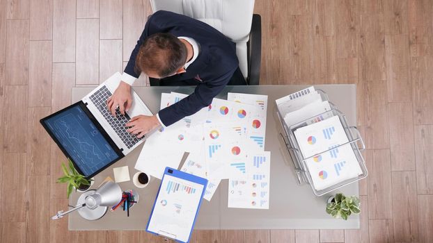 Top view of businessman typing company startegy on laptop computer while working at management investments project in startup office. Manager in suit analyzing management statistics