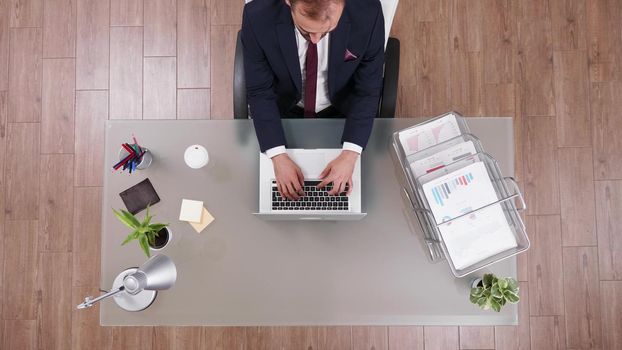 Top view of successful businessman in suit typing marketing strategy on laptop working in startup business company office. Executive manager analyzing financial profit at workspace