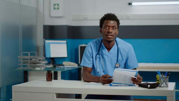 Man nurse talking on video call technology while sitting at desk in professional cabinet. Medical assistant using online remote communication and conference via internet for telemedicine