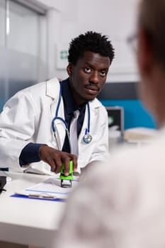 Medic of african american ethnicity holding stamp to sign documents for patient sitting at desk. Black man with doctor occupation using tool on paper files for chekup at healthcare clinic