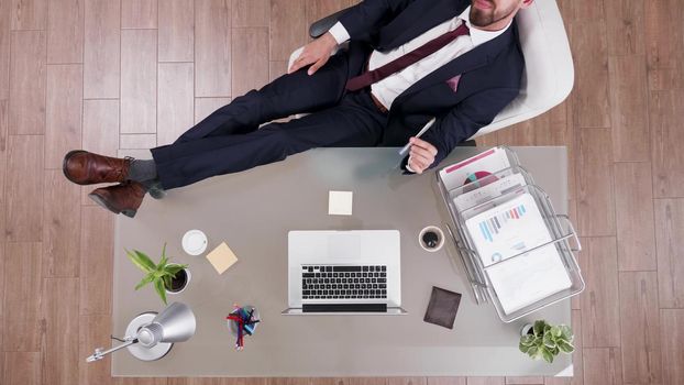 Top view of businessman in suit staying relaxed with feet on office desk thinking at financial profit. Executive manager working in startup company office at management investments