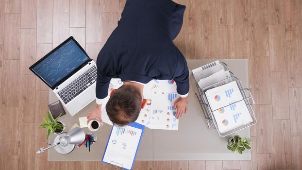 Top view of businessman in suit taking coffee while analyzing management statistics planning company investments. Executive manager working at marketing strategy in startup corporate office