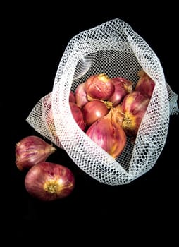 Red onions in mesh bag and some on floor isolated on black background