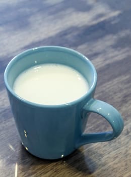 Milk in a blue cup on the wooden and top glass table