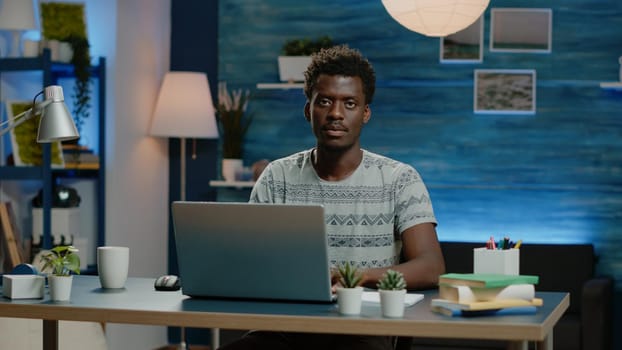 Entrepreneur using laptop for remote online work. Corporate worker typing on keyboard, working from home on device. Man smiling and looking at camera while doing business project