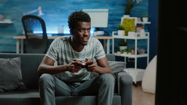 Black man using controller and console to play video games on television for free time activity. African american person playing game with joystick on TV for entertainment. Adult having fun