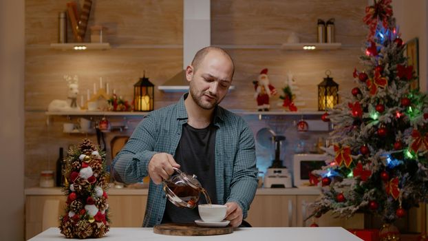 Young man talking on video call with family for festive season. Adult using online conference on internet for christmas eve celebration in decorated kitchen. Holiday conversation