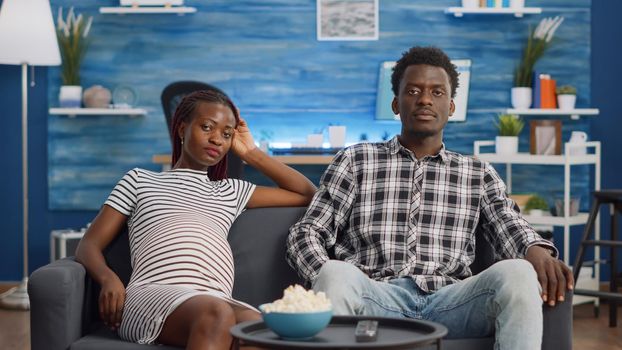 Black married couple with pregnancy talking on video call conference while sitting on living room sofa. African american people expecting baby and using online remote communication