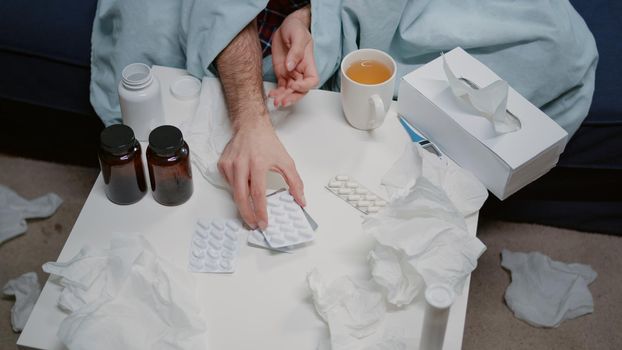 Top view of table with medicaments, bottles of pills and tea for ill man with flu and cold. Sick adult looking at tablets with capsules to cure virus symptoms at home. Person with illness