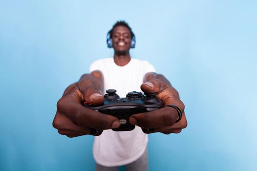 Person showing controller to play video games while wearing headset. Young adult playing game with joystick and listening to music on headphones. Modern man having fun with technology.