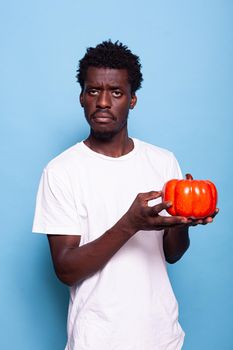 Vegan person holding red bellpepper in hand. Man presenting raw vegetable to camera for healthy diet and organic nutrition. Young adult showing veggie in palm while looking at camera