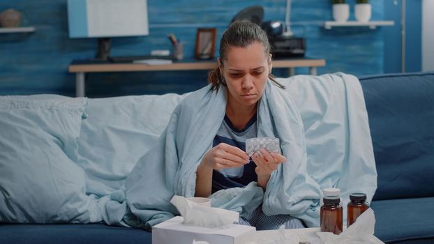 Sick person looking at capsule tablets and bottle of pills for disease treatment. Woman in blanket reading labels of medicaments against cold and flu. Adult with prescription medicine