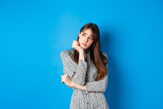Lonely romantic girl in dress, looking left at logo with sad and gloomy face, standing on blue background.